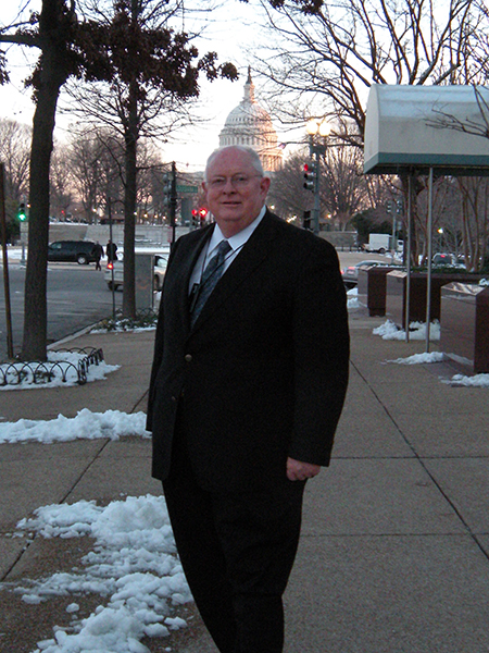A man in a suit stands on the street in front of the United States Capitol.