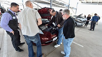 Four people look under the hood of a PEV at an electric vehicle ride and drive.