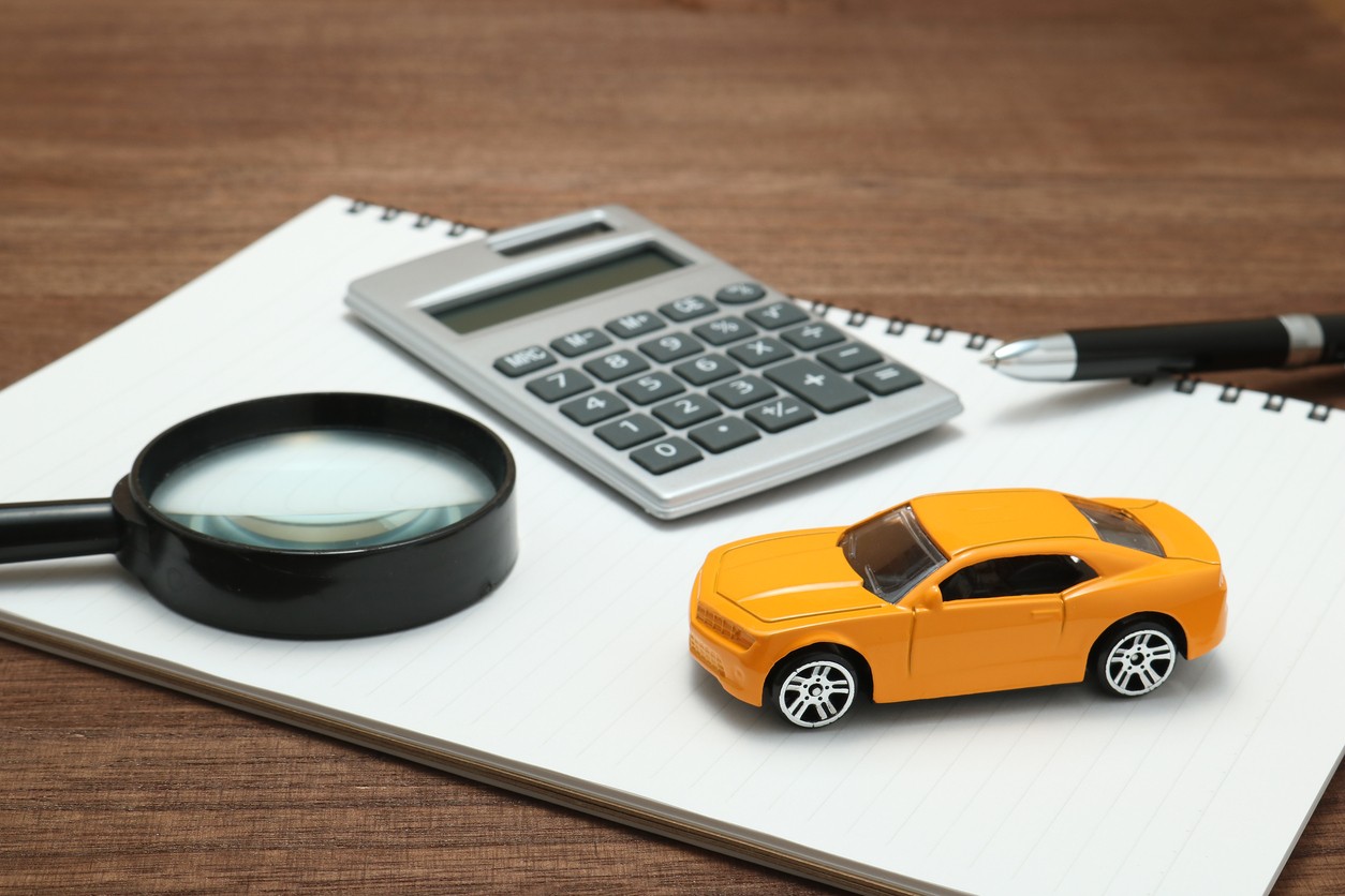A photo of a toy car, calculator, and magnifying glass sitting on a piece of paper.