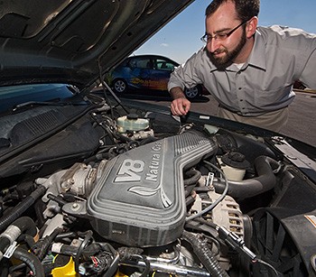 A photo a man in glasses standing over the open hood of a car with a natural gas engine.