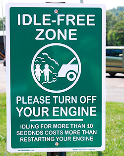A photo of a green sign with white writing and a graphic showing a car with exhaust spewing out the tailpipe onto people.