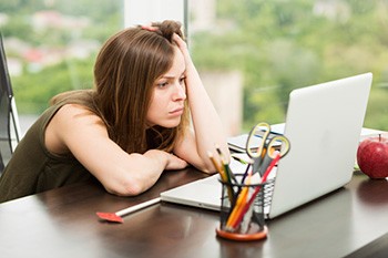 Poto of a woman staring at a computer with her head in her hands.